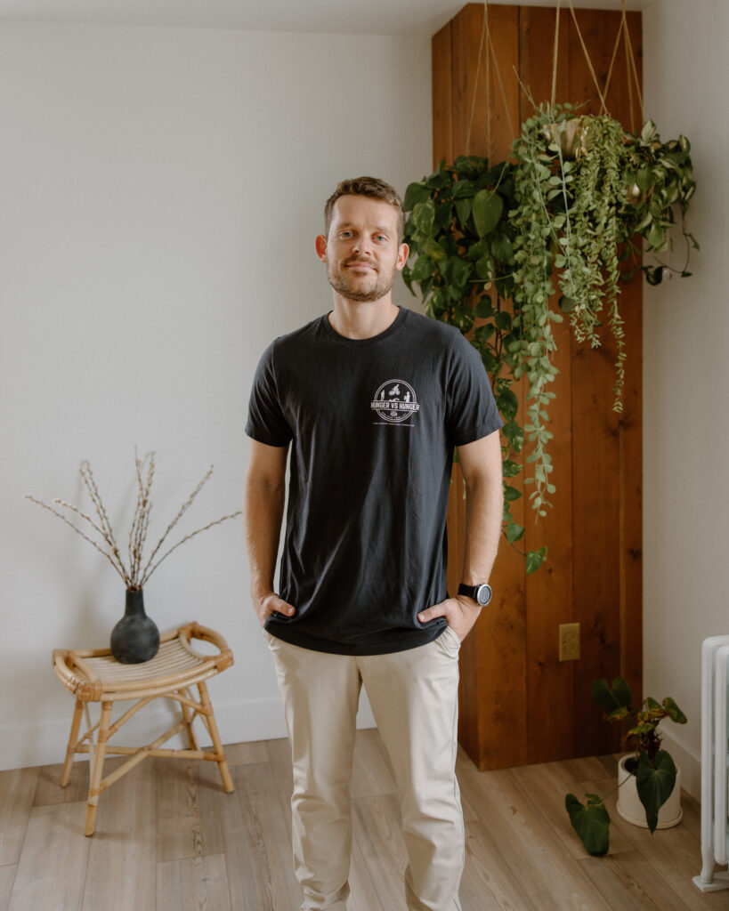 ethan hunger wearing a black tshirt, khaki pants, standing with his hands in his pockets
