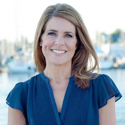 rita blair wearing a blue shirt standing in front of the marina, smiling